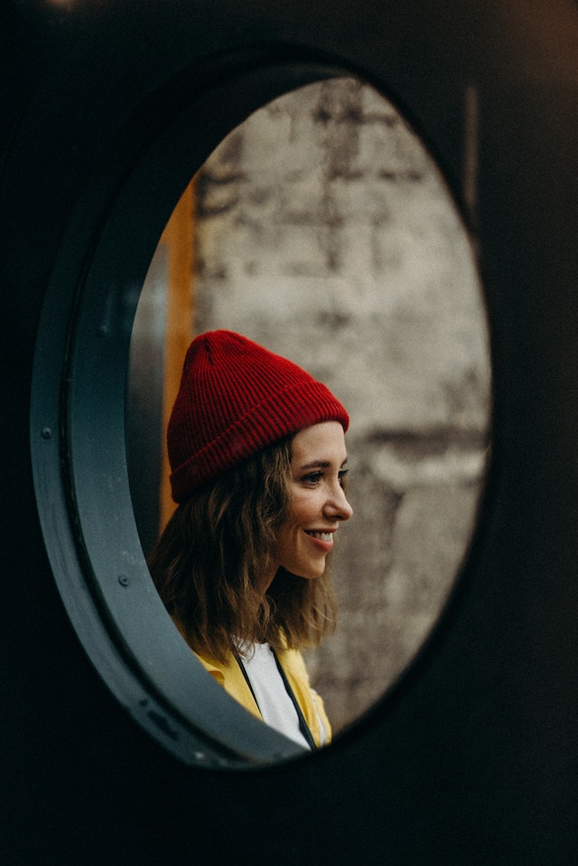 Lächelnde Frau mit roter Mützen im Spiegel.